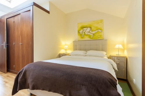 Quarto moderno no Bairro Alto de Lisboa com paredes amarelas, cama de casal, manta escura, luminárias de cabeceira e guarda-roupa em madeira.
