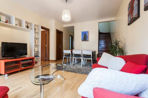 Sala de estar de apartamento moderno em Lisboa com sofá vermelho, TV, área de refeições e assoalho em madeira