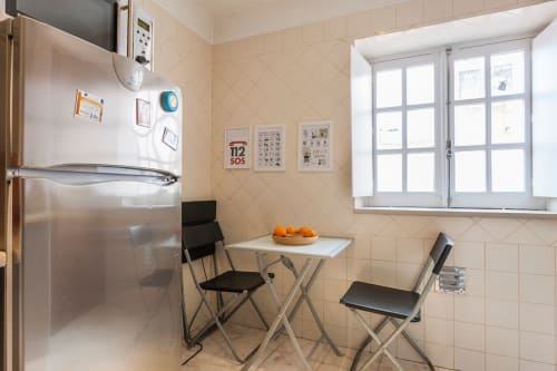 Cozinha compacta com eletrodomésticos em aço inoxidável, mesa de jantar com cadeiras e janela em apartamento em Lisboa