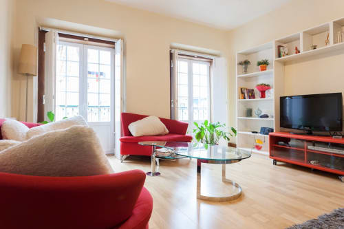 Sala de estar de apartamento moderno em Lisboa com sofás vermelhos, mesa de café em vidro e prateleiras embutidas com TV