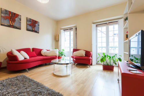 Sofá vermelho moderno e poltrona em sala amarelo brilhante do apartamento duplex Bairro Alto em Lisboa com acesso à varanda
