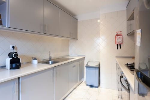Cozinha moderna branca em apartamento de Lisboa com armários cinzentos, eletrodomésticos de aço inoxidável e painel de azulejos diagonal