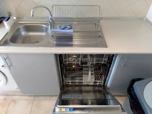 Pia de aço inoxidável e máquina de lavar louça aberta em apartamento em Lisboa, mostrando eletrodomésticos modernos e escorredor de pratos.