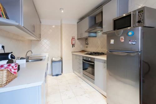 Cozinha moderna em apartamento lisboeta com eletrodomésticos em aço inoxidável, armários brancos, fogão a gás e pavimento em azulejo