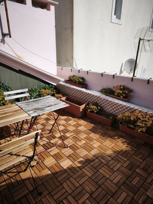 Terraço ensolarado no Bairro Alto com assoalho em espinha de peixe, mesa de refeições, flores em vasos e paredes rosa.