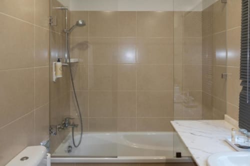 Banheiro moderno com chuveiro tipo walk-in, paredes revestidas de azulejos bege e bancada em mármore branco na Quinta de Anterronde em Arouca