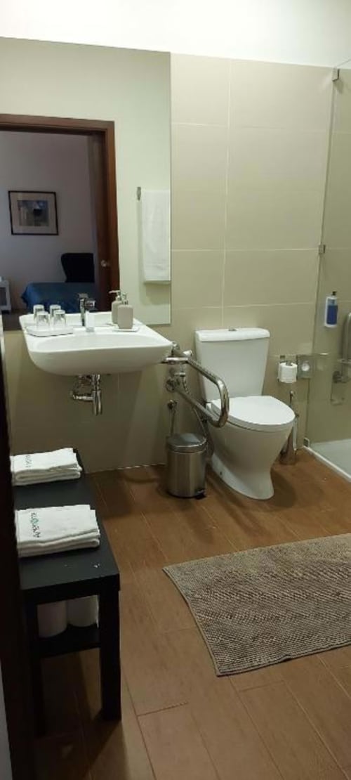 Banheiro moderno na Suite Familiar da Quinta de Anterronde com lavatório branco, vaso sanitário, piso de madeira e azulejos creme