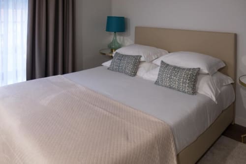 Quarto moderno com cabeceira bege, travesseiros brancos, almofadas estampadas em tons de azul-petróleo e vistas para as montanhas da Quinta de