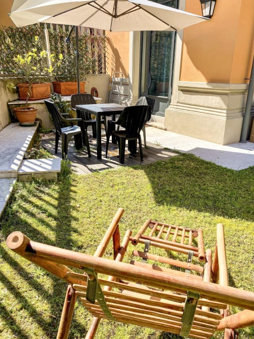 Terrazza con vista giardino dell'esclusivo appartamento di Verona: tavolo da pranzo, ombrellone, lettini in legno e vegetazione rigogliosa