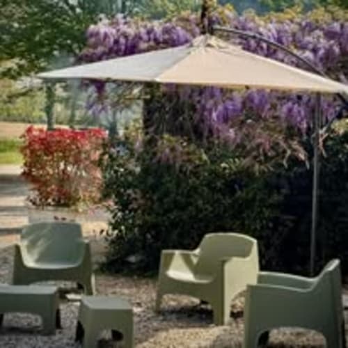 Area lounge dell'Agriturismo Villa Mocenigo con ombrellone beige, sedie verdi e glicine viola in fiore