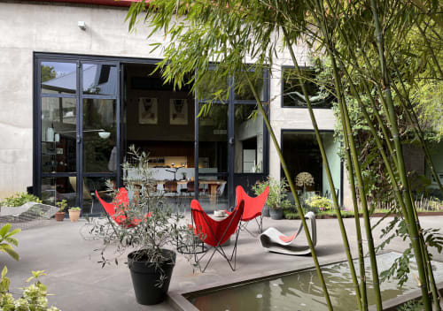 Modern patio at La Porte Rouge Roubaix with red butterfly chairs, bamboo plants, and glass doors opening to the interior