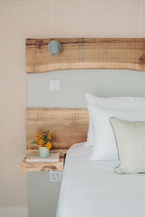 Quarto moderno em M'ar Puro com cabeceira de madeira, almofadas brancas, flores amarelas e prateleira integrada à cabeceira em Santo