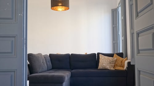 Sofá moderno oscuro con cojines dorados en apartamento del Eixample barcelonés, lámpara colgante, diseño minimalista luminoso