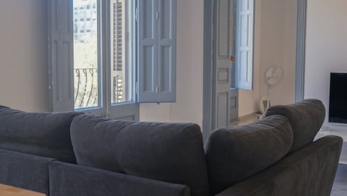 Sofá gris oscuro en apartamento del Eixample de Barcelona con vistas de la ciudad a través de las puertas del balcón