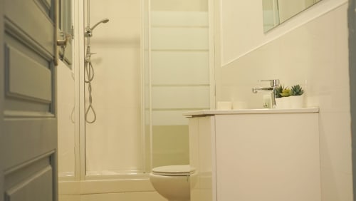 Baño moderno en apartamento del Eixample de Barcelona con ducha tipo walk-in, inodoro y acabados en azulejos blancos