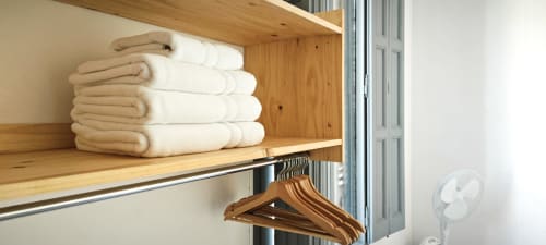 Toallas de crema cuidadosamente apiladas en estantería de madera con perchas de madera en apartamento de Barcelona