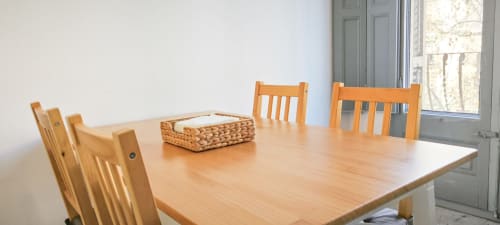 Comedor luminoso en apartamento Barcelona Eixample con mesa de madera, sillas y cesta tejida decorativa