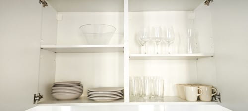 Armario de cocina blanco con vajilla, cristalería y tazas organizadas en apartamento BCNMADflats Barcelona