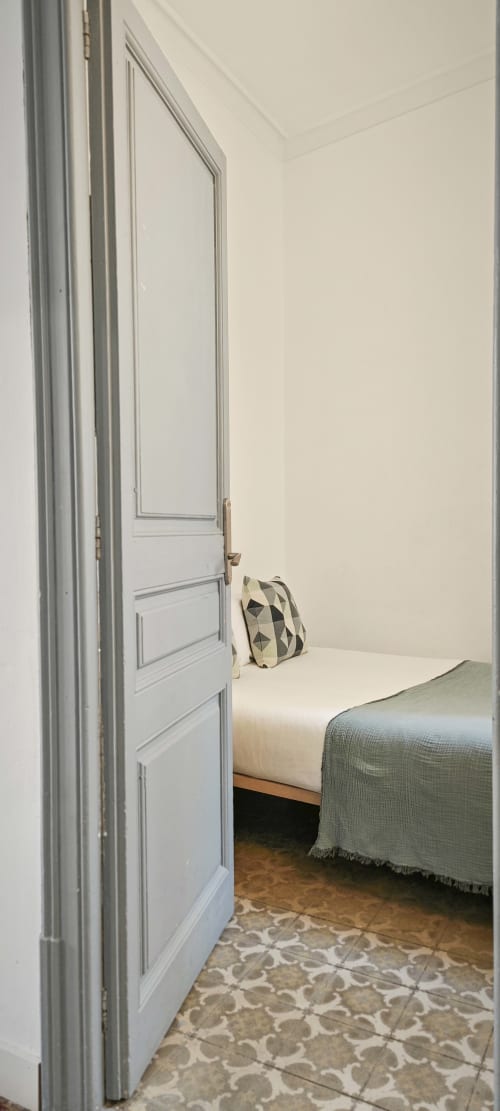 Dormitorio luminoso en apartamento de Barcelona Eixample con puerta blanca, cama, almohada geométrica y suelo con patrón en BCNMADflats.