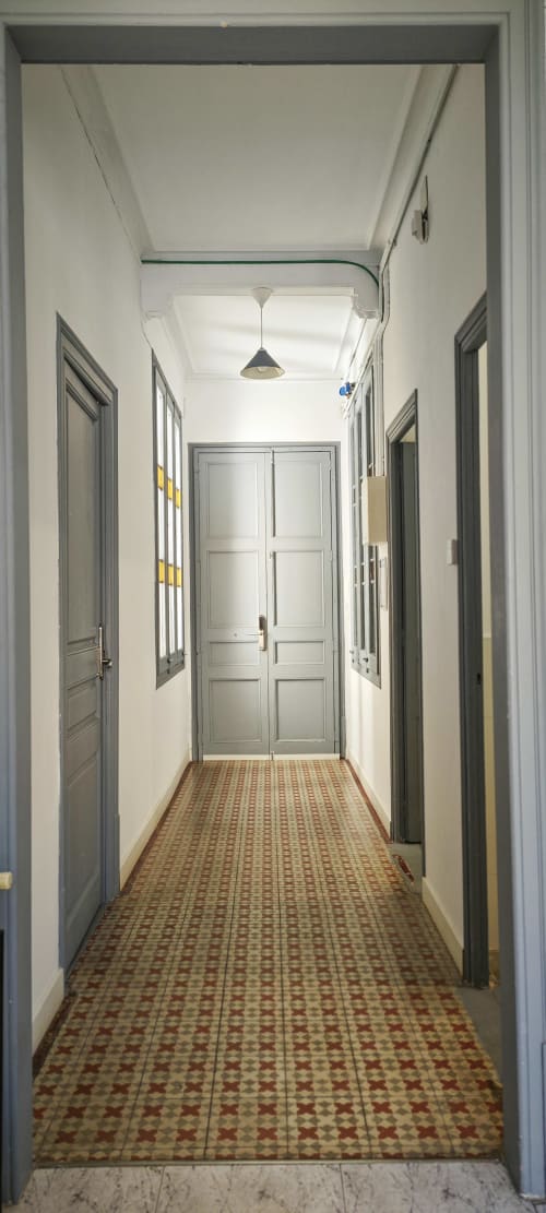 Largo pasillo en apartamento del Eixample de Barcelona con suelo de baldosas estampadas, puertas grises e iluminación de péndola