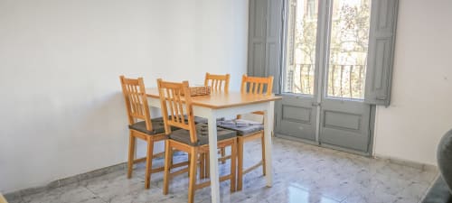 Comedor luminoso en apartamento de Barcelona Eixample con mesa de madera, sillas y vistas de la ciudad a través de las puertas del balcón.