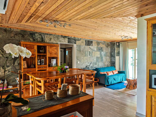 Intérieur spacieux du gîte avec poutres en bois, table de salle à manger, mur en pierre et canapé bleu à La Kaz 57