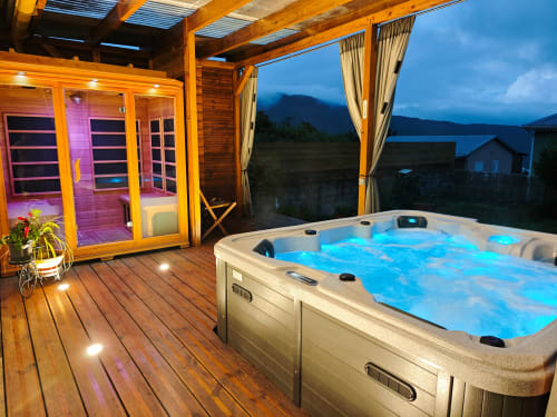 Luxueux bain à remous sur terrasse en bois à La Kaz 57, La Plaine des Palmistes, avec sauna et vue sur les montagnes au crépuscule