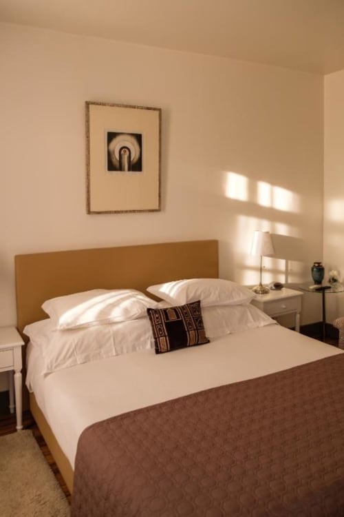 Quarto luminoso na Quinta de Anterronde com cabeceira mostarda, roupa de cama branca, quadros na parede e vista para as montanhas