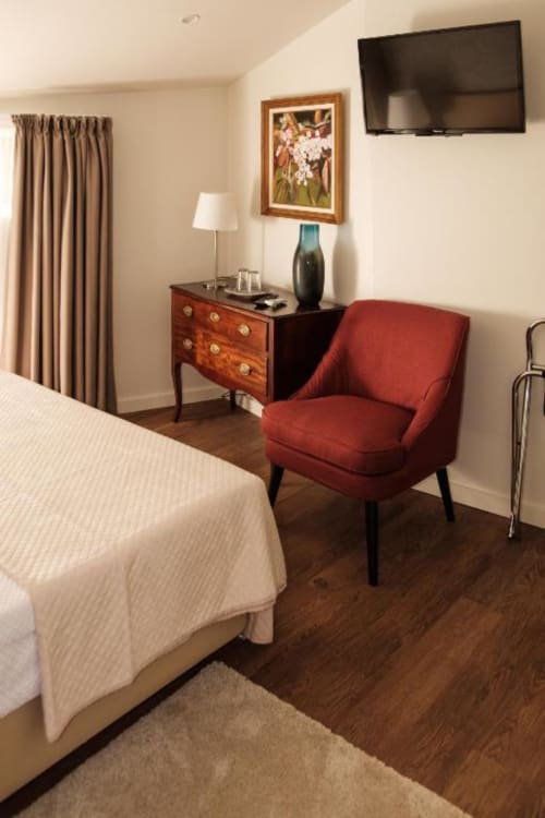 Suite elegante da Quinta de Anterronde com poltrona vermelha, cômoda em madeira, TV de tela plana e roupa de cama creme
