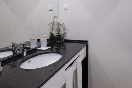 Banheiro moderno da Suite Standard na Quinta de Anterronde, com bancada em granito preto, pia branca e orquídea