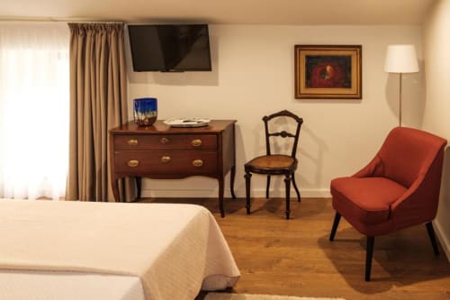 Quarto elegante da Quinta de Anterronde com cama, escrivaninha de madeira, poltrona vermelha e TV de tela plana