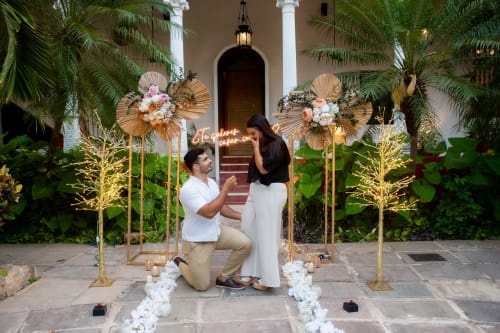 Proposta di matrimonio nella corte romantica di Villa Merida con palme, decorazioni dorate e archi floreali ornamentali