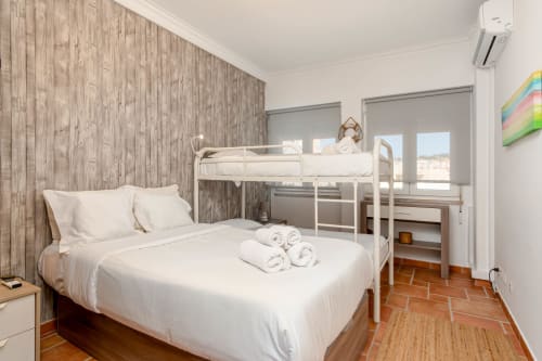Bright bedroom at Republica do Sul hotel in Aroeira with queen bed, bunk beds, wood accent wall and sea view balcony