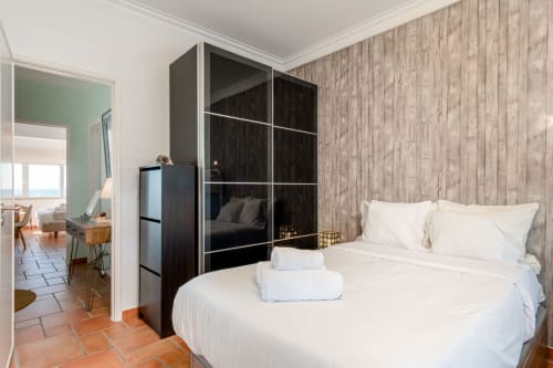 Ocean view apartment bedroom at Republica do Sul with sea-view, white bedding, wooden accent wall, modern black wardrobe, and
