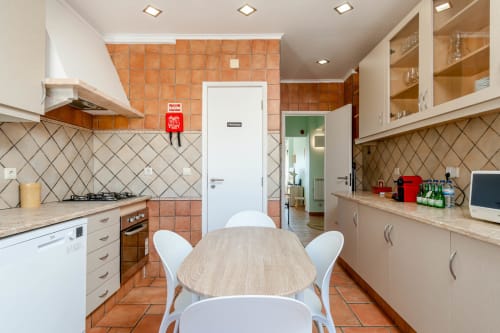Modern kitchen with orange tile backsplash, white cabinetry, and dining table in Republica do Sul apartment, Charneca da