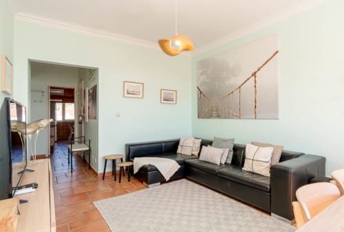 Modern living room with black leather sectional sofa, wood furniture, and sea view artwork in Aroeira apartment rental,