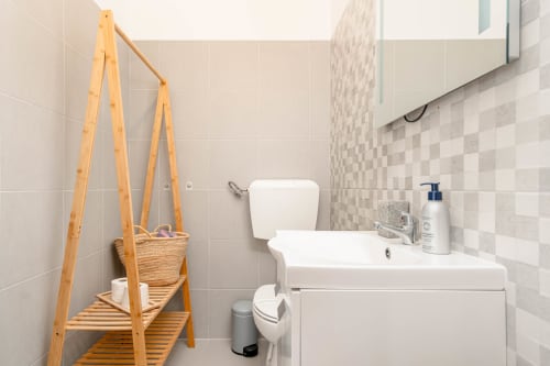 Modern bathroom with white sink and toilet, beige tiled walls, wooden ladder shelf with basket, at Republica do Sul hotel in