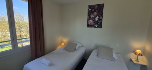 Chambre double aux Genêts d'Or à Trévé avec deux lits simples, lampes de chevet et vue sur la ville
