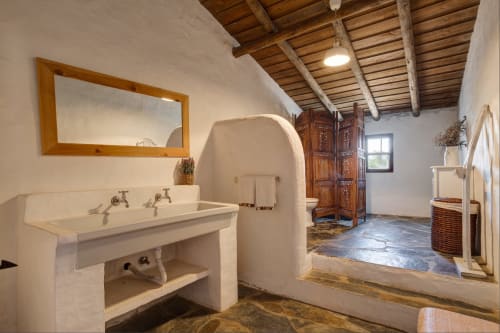 Banheiro espaçoso da villa Vale Clara, Alandroal, com paredes brancas curvas, vigas de madeira no teto, pia e espelho vintage