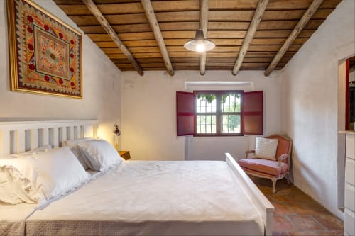 Quarto rústico da villa Vale Clara em Alandroal com roupa de cama branca, vigas de madeira aparente, persianas bordô e decoração tradicional