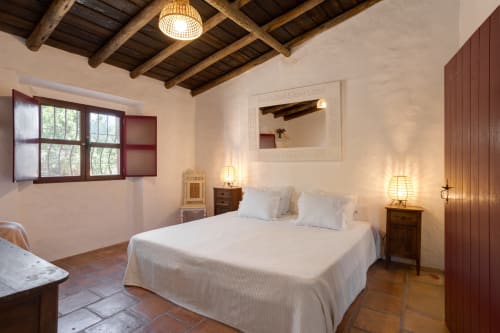 Quarto rústico na villa Vale Clara em Alandroal com teto de vigas, cama branca, mesas laterais de madeira e iluminação acolhedora