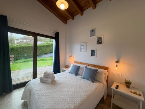 Moderna habitación con vistas al jardín en El Respigu, Cangas de Onís. Cama de madera, lámparas colgantes y puertas de patio con vistas al verde