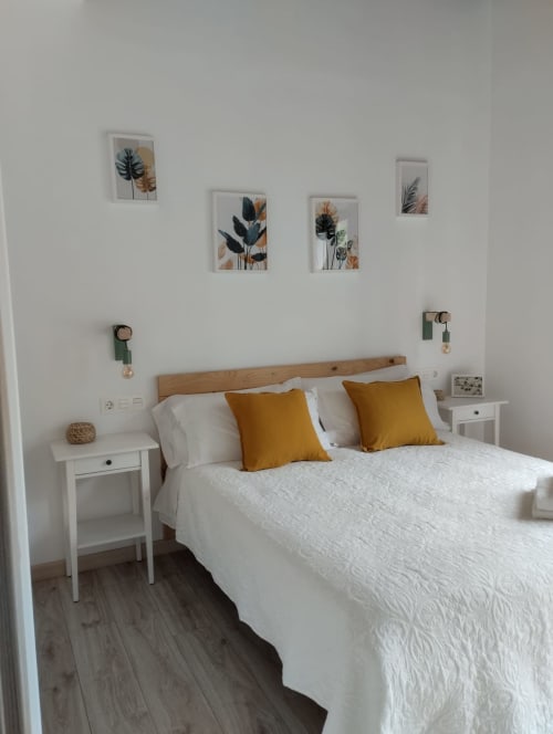 Dormitorio luminoso en Apartamentos El Respigu con cama de madera, ropa de cama blanca, almohadas amarillas y decoración botánica