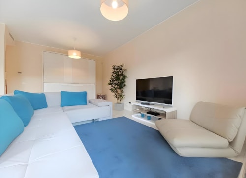 Sala de estar clara em Portimão com sofá azul e branco, TV, poltrona creme e móveis modernos