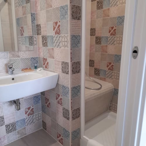 Modern bathroom with patterned tile walls, white sink, and bathtub at L'attico di Matilde B&B in Siracusa, Italy
