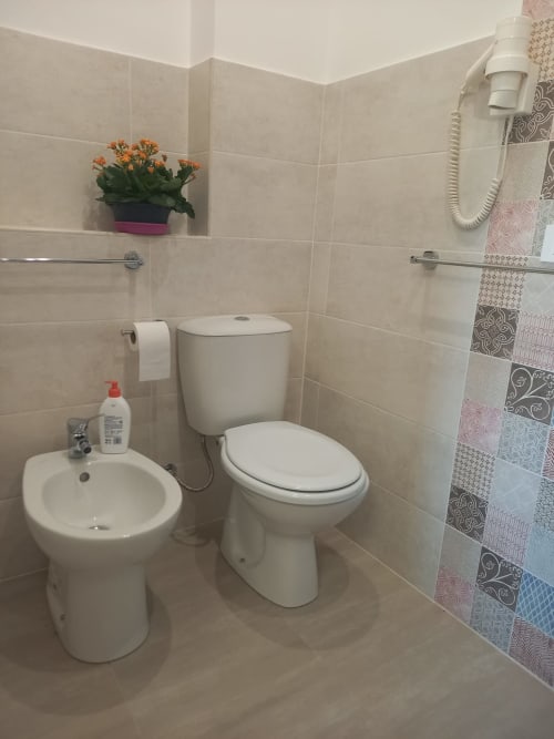 Clean bathroom in L'attico di Matilde, Siracusa. White toilet, bidet, sink with decorative patterned shower curtain and