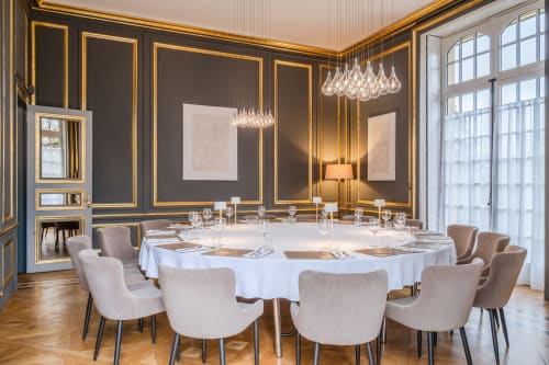 Élégante salle à manger d'Ô Château à Hayange avec table ronde, chaises capitonnées, murs ornés de dorures et lustre en cristal