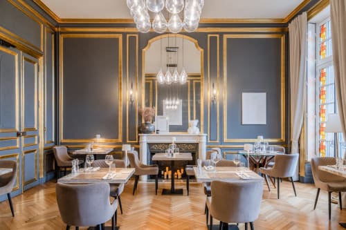 Élégante salle à manger de l'hôtel Ô Château à Hayange avec murs dorés, lustres et tables raffinées