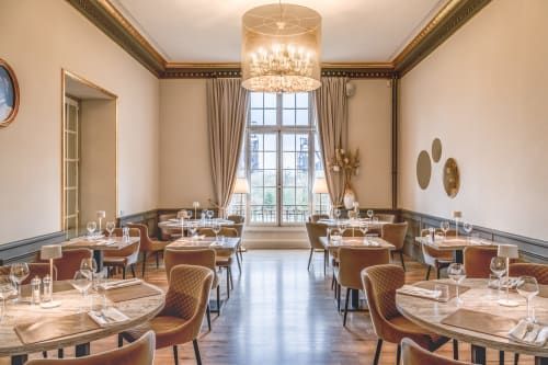 Élégante salle à manger du restaurant Ô Château à Hayange avec tables rondes, chaises modernes, lustres en cristal et baies vitrées