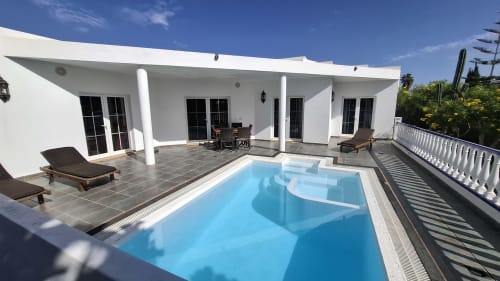 Villa moderna blanca con piscina privada, tumbonas y zona de comedor con vistas al jardín en Puerto Calero, Las Palmas